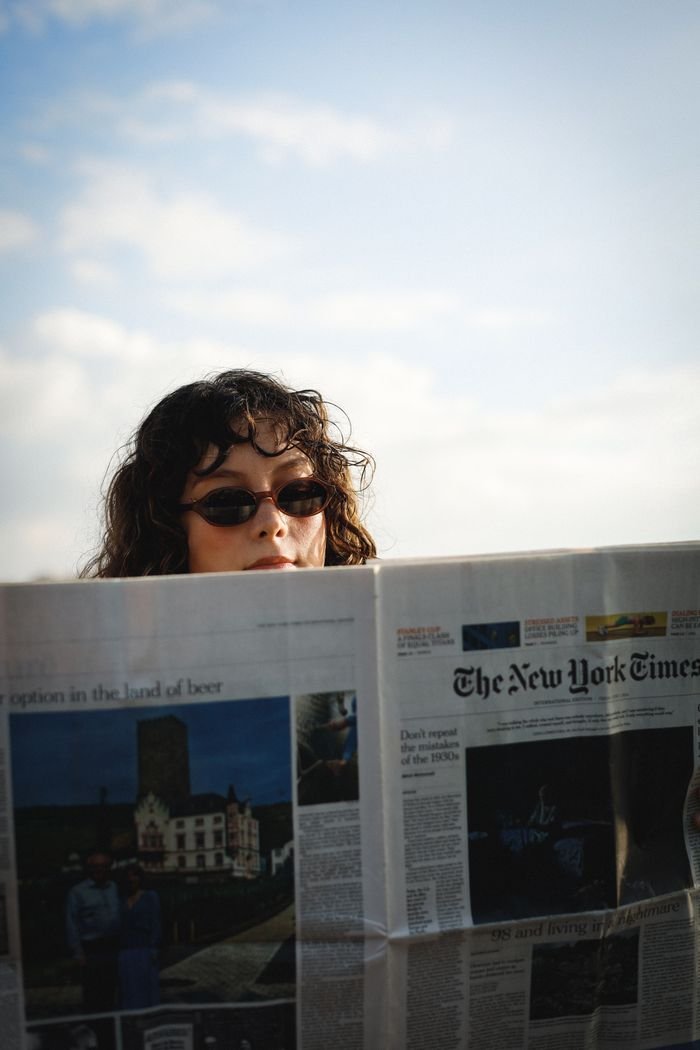 Individual wearing sunglasses enjoys a newspaper under clear skies. Relaxed outdoor atmosphere.